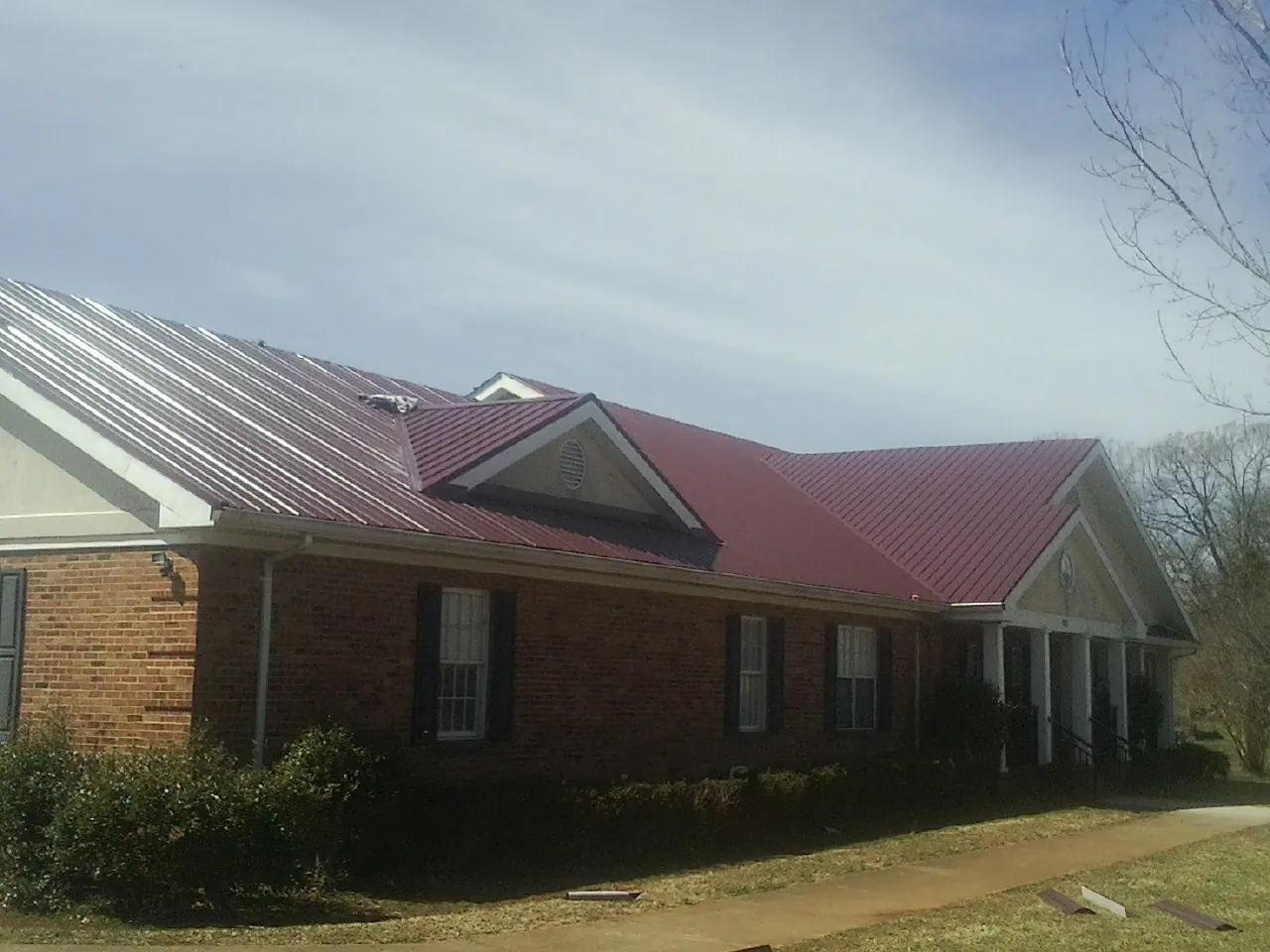 Red metal roof with gabled entries on a long brick building, from a Hail Damage Roof Repair job in Grand Coulee