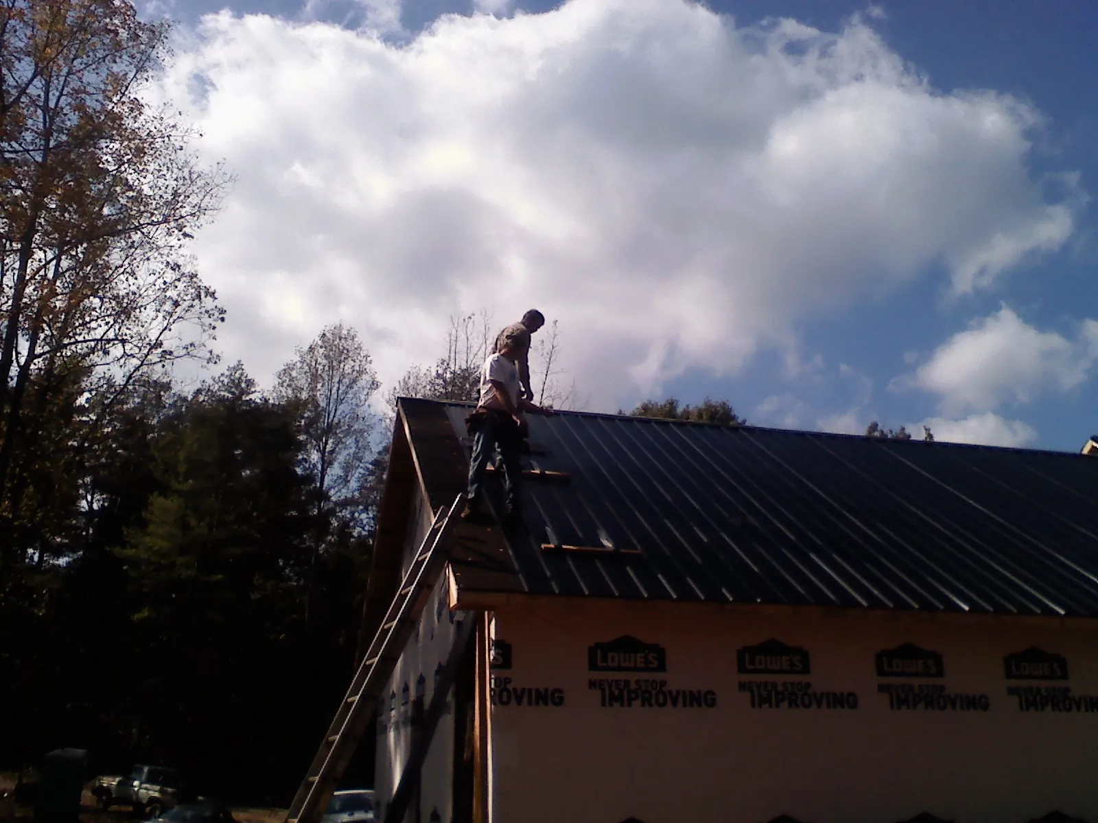 Roofer fastening dark metal panels high against a cloudy sky, from a Roof Inspection job in Grand Coulee