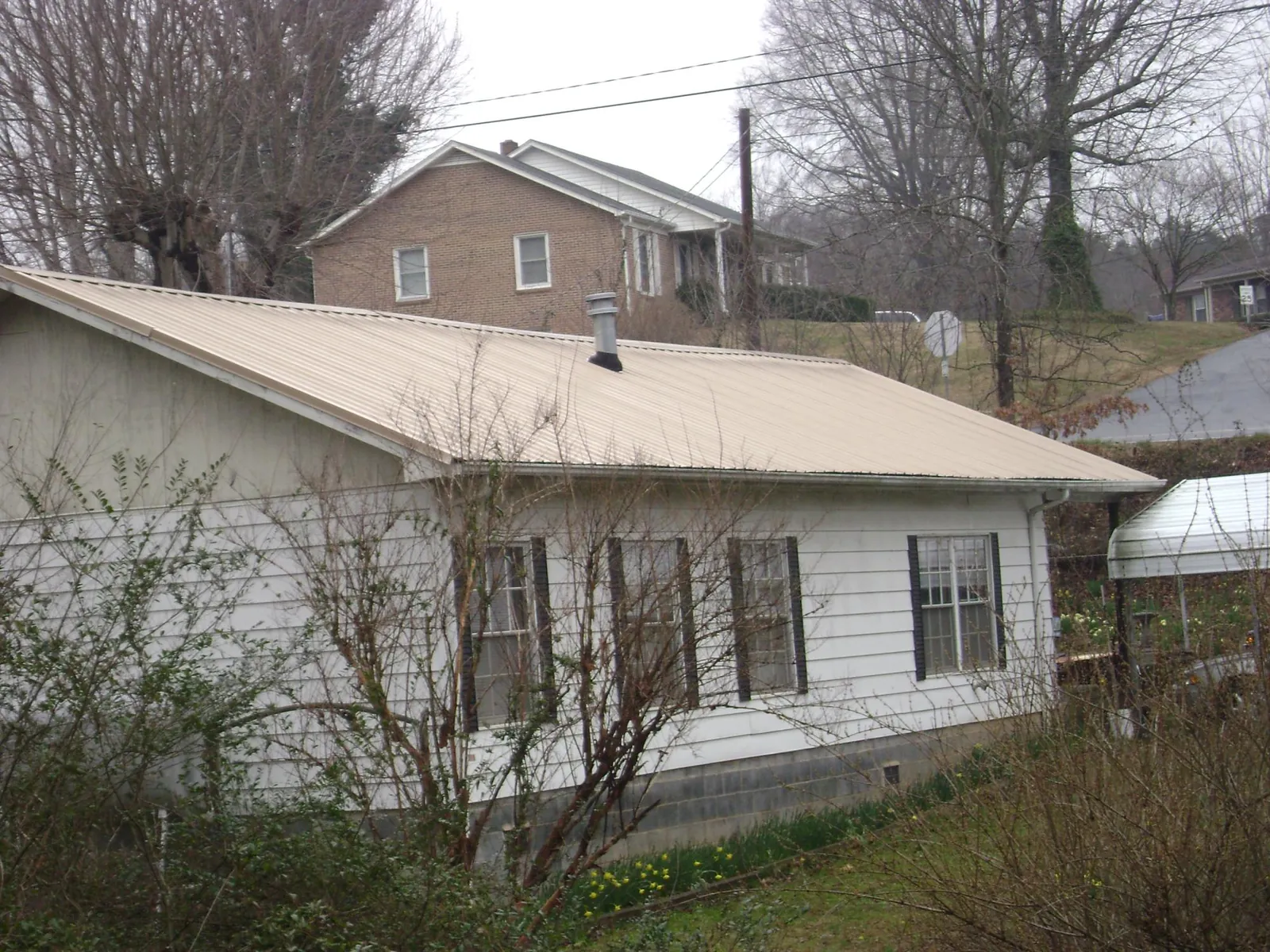 Tan metal roof on a white sided house set into a hillside — Commercial Roofing by Roofing Brothers in Grand Coulee